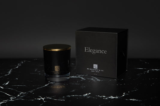 a luxury candle in a black glass with a black box beside and a dark background