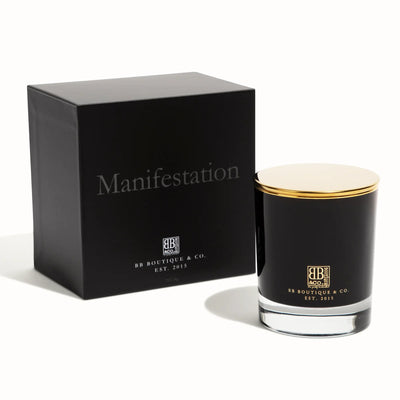 Product Photography by BB Boutique & Co. showing a sleek black Manifestation candle with a gold lid in a clear bottom glass jar beside its matching matte black box with glossy Manifestation text and gold BB Boutique & Co. logo on a clean white studio backdrop