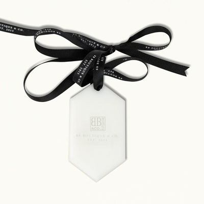 White hexagonal BB Boutique & Co brand tag with a subtle grey logo and text hanging from a black grosgrain ribbon tied in a bow with repeating white BB Boutique & Co Est 2015 text against a clean white background