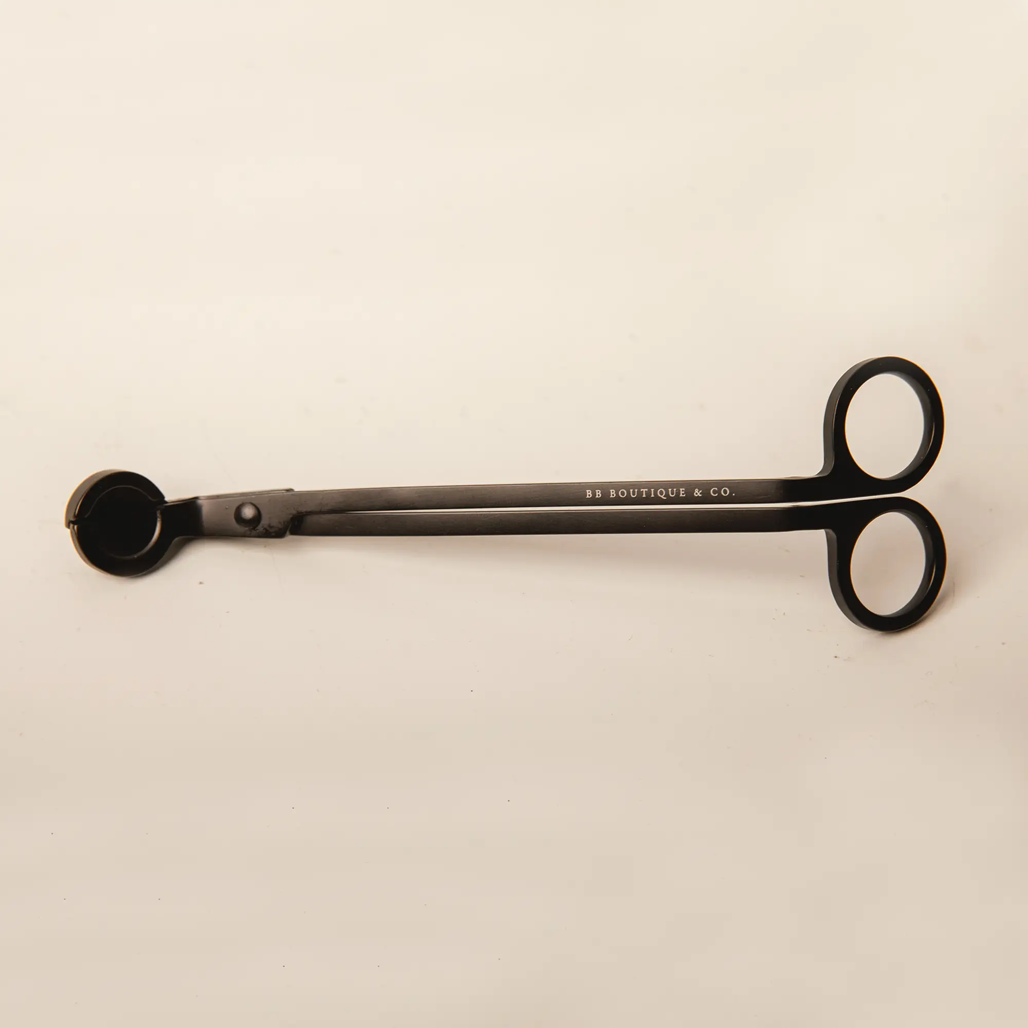 Product by BB BOUTIQUE & CO. a sleek matte black candle wick trimmer featuring white brand lettering, circular finger holes, and a curved clipping tray against a soft beige studio backdrop