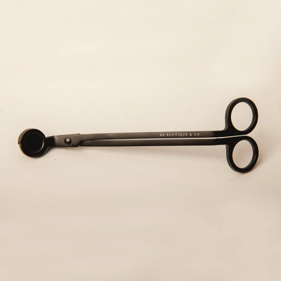 Product by BB BOUTIQUE & CO. a sleek matte black candle wick trimmer featuring white brand lettering, circular finger holes, and a curved clipping tray against a soft beige studio backdrop