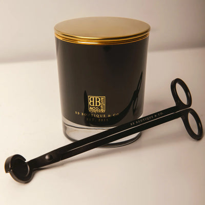 BB Boutique & Co. product photography showcasing a luxurious black candle jar with a shining gold lid and prominent gold brand logo next to a matching matte black wick trimmer on a clean white studio background