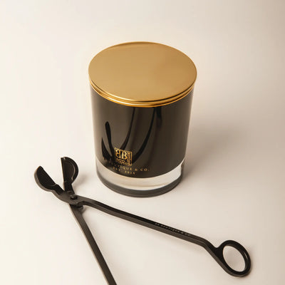 Product photo featuring a sleek black glass candle with a shiny gold lid and BB Boutique & Co EST 2015 branding alongside a matching matte black wick trimmer presented on a minimalist white studio background
