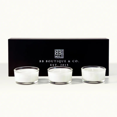 Product photography of three white BB Boutique & Co. votive candles in clear glass holders positioned in front of a sleek black gift box displaying the "BB Boutique & Co. EST. 2015" logo in white on a clean white studio background