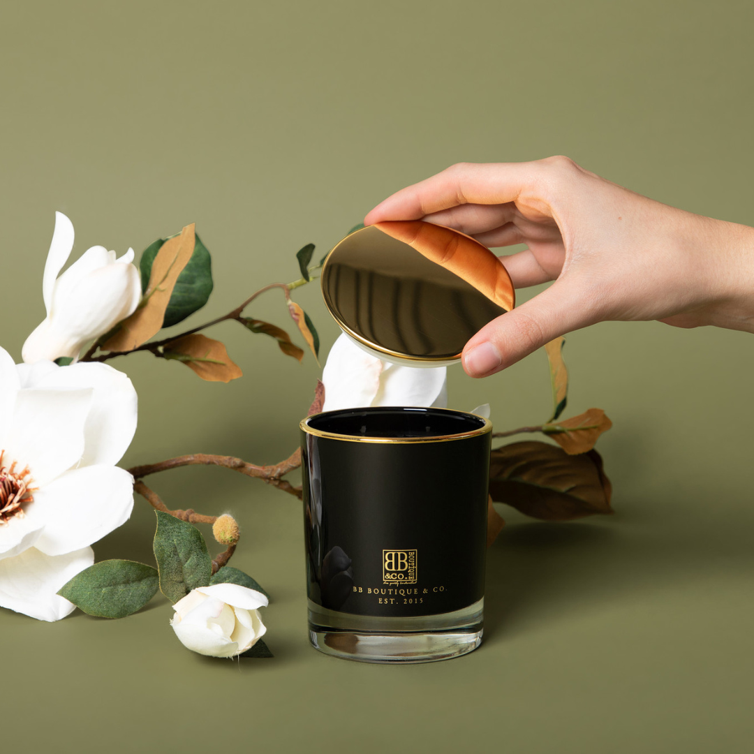 Hand holding black candle vessel with gold lid.